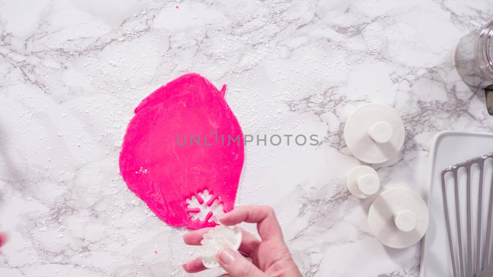 Flat lay. Step by step. Cutting out snowflakes with cookie cutters out of pink fondant on a marble counter.