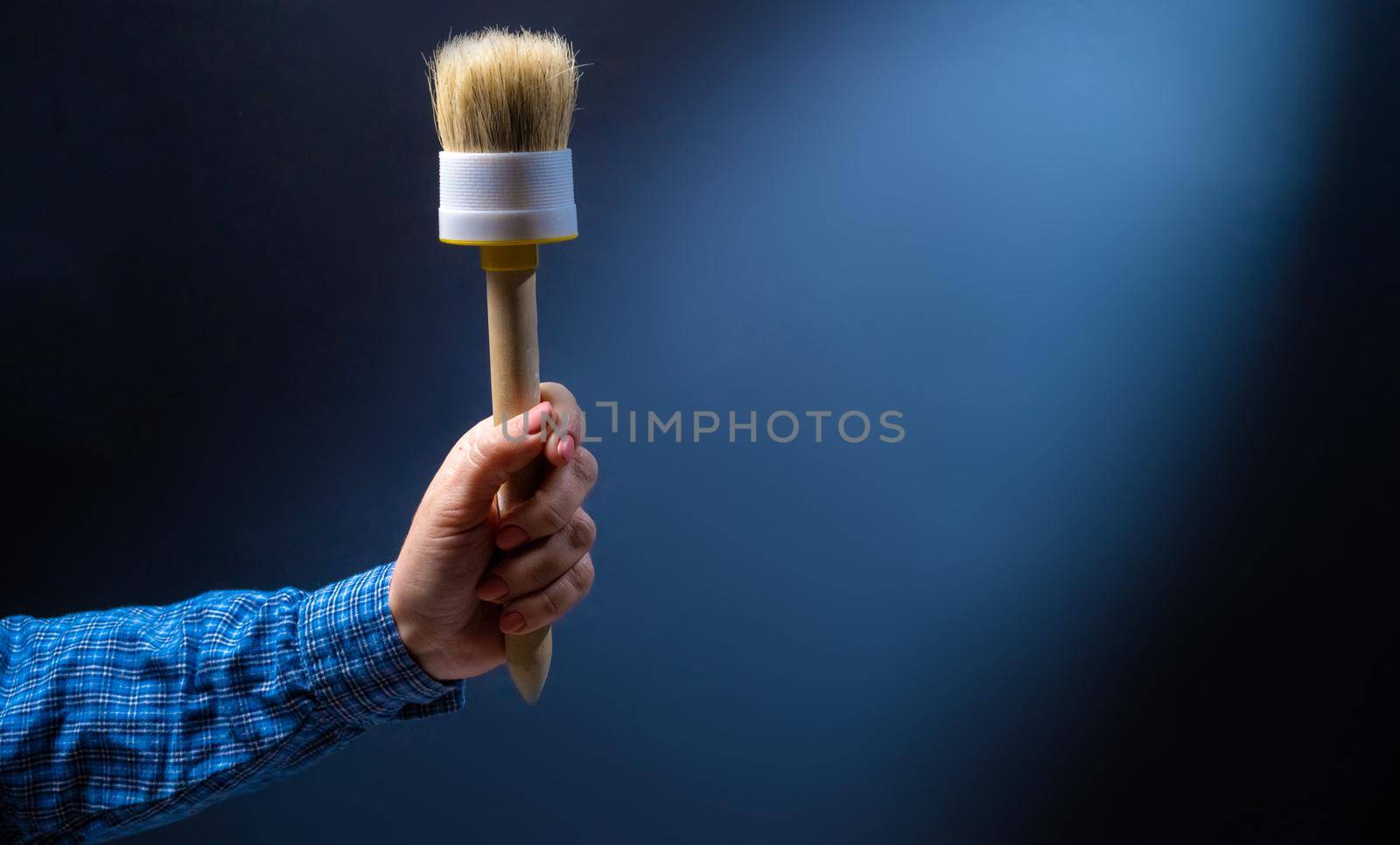Hand holding brush for interior renovation on blue background. Person with paintbrush decoration tool