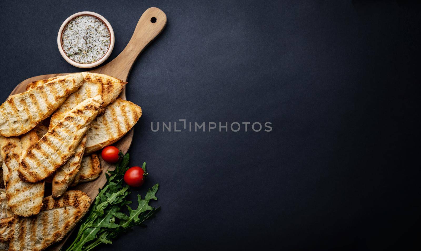 Toasts with cherry tomatoes, arugula and salt on wooden board on background with copyspace. Sliced toasted bread with vegetables and herbs