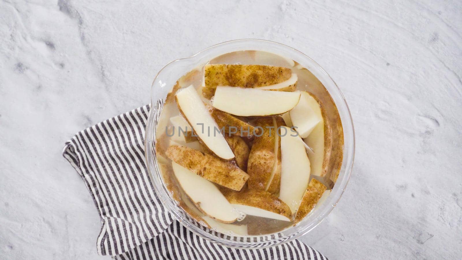 Flat lay. Step by step. Soaking potato wedges in a bowl of water to prepare baked potato wedges with spices.