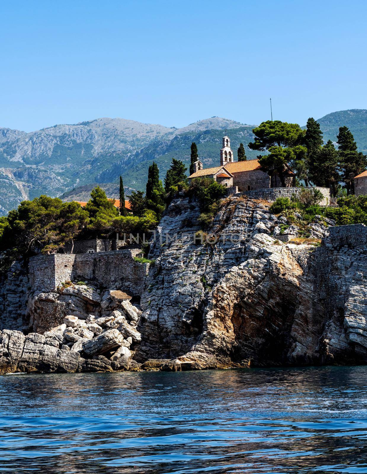 Scenic town on rocks in Montenegro, view from Adriatic sea in summertime. Beautiful Mediterranean architecture with mountains in sunny day