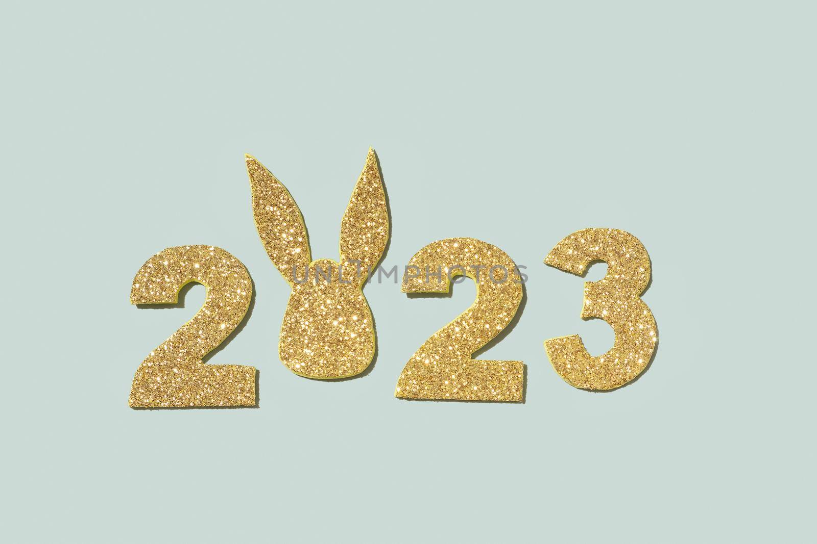 Shiny gold numbers 2023 with rabbit ears symbol new year on a pastel green background.