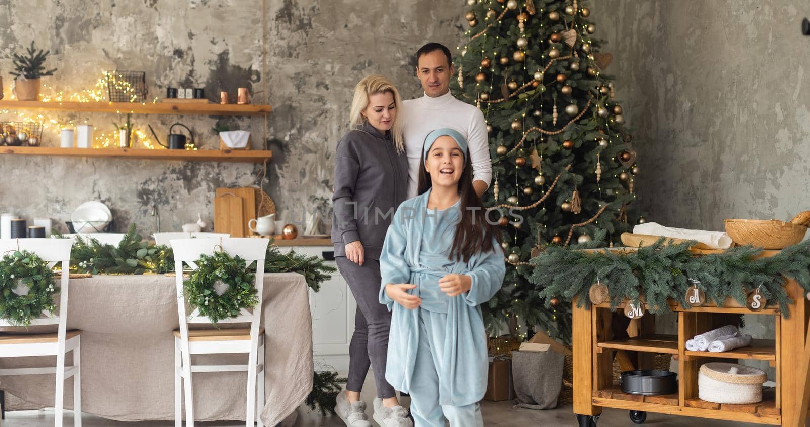 beautiful Christmas tree at home. Parents presenting gift box to charming daughter
