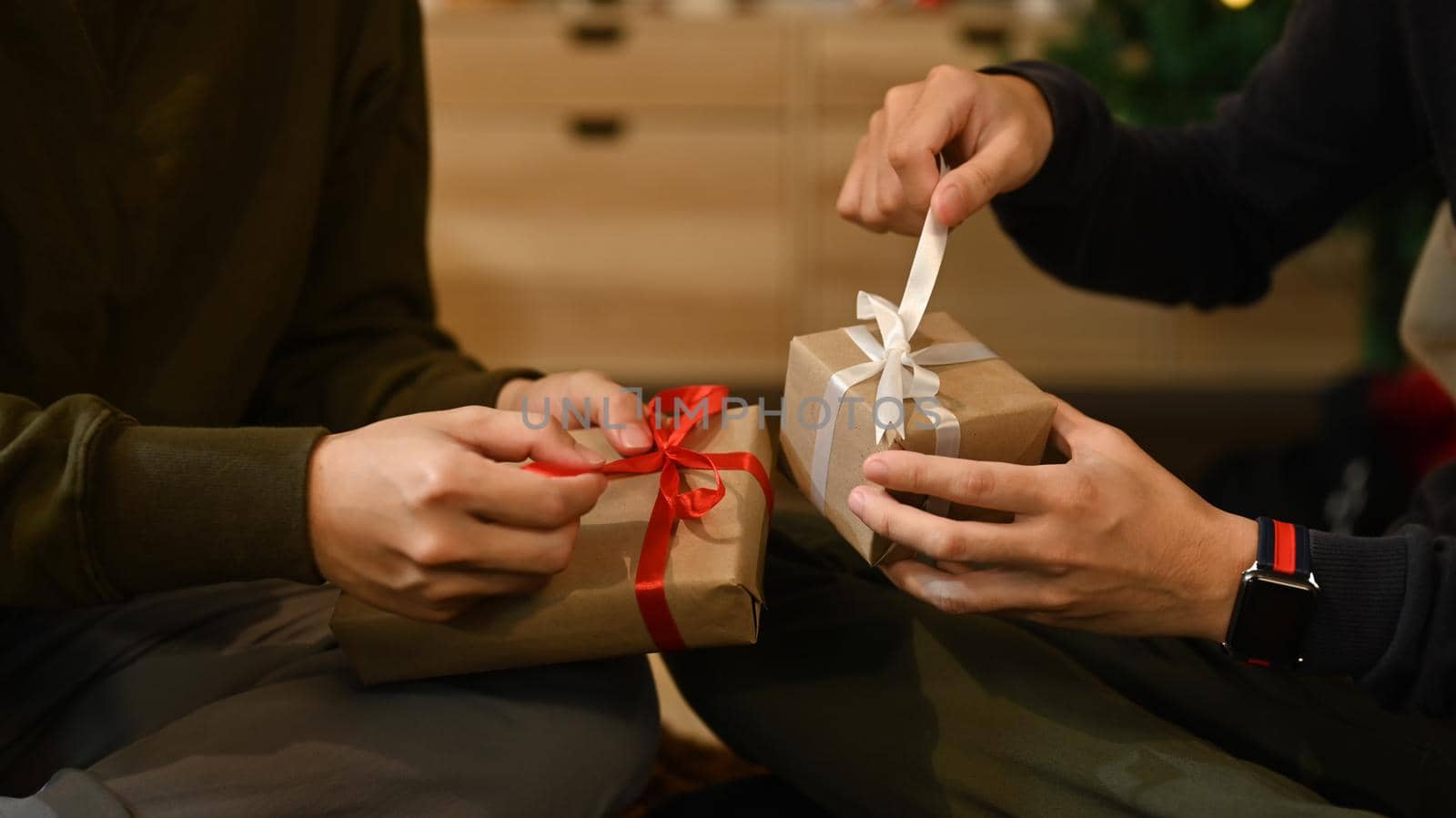 Cropped image of men celebrating Christmas, New Year at home together and exchange presents. Holidays and celebration concept.
