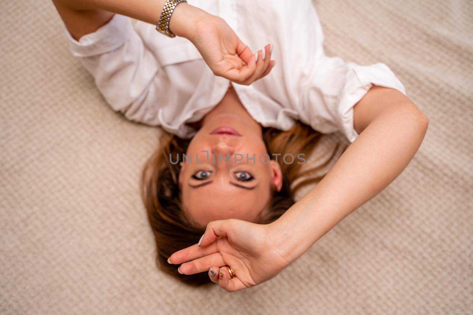 The woman lies on the bed on her back, top view. She looks straight ahead, wearing a white shirt.