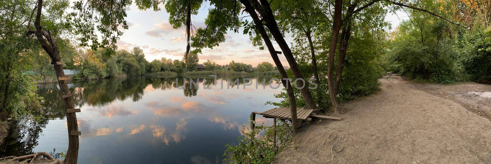 Summer forest lake with mirror reflection of trees and vegetation near the village.