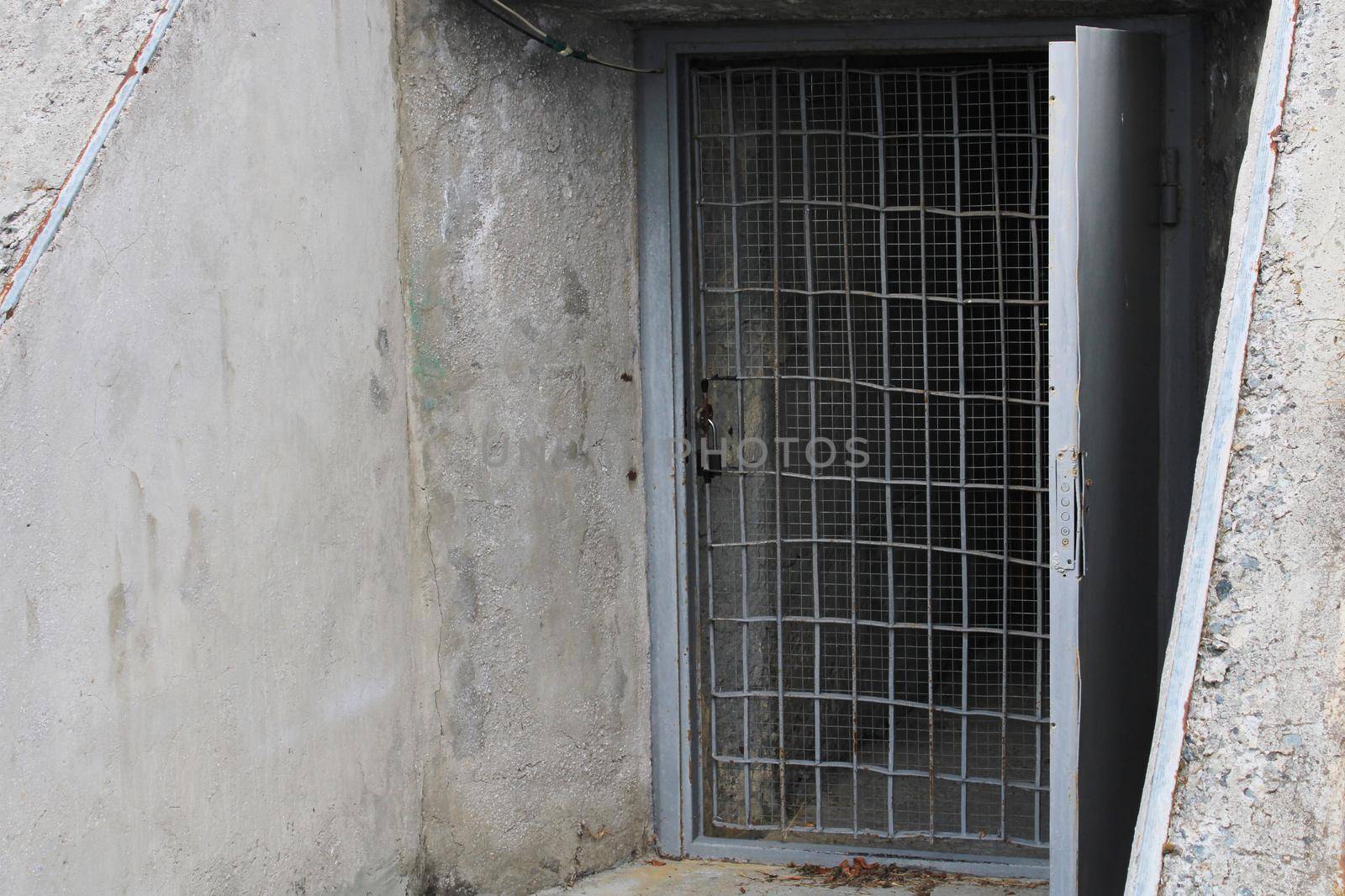 Open door to the cellar with bars in an old stone building.