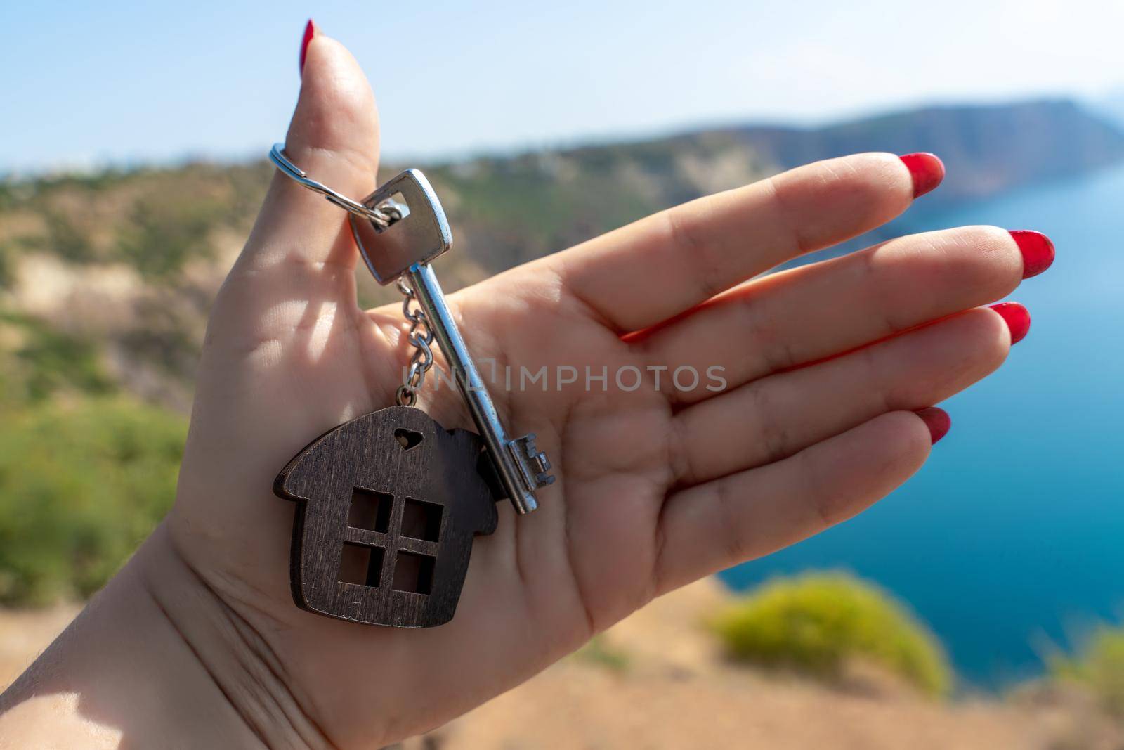 Keys with a keychain in the shape of a house in a female hand against the backdrop of the sea. The concept of buying a house, apartment, real estate, young family, mortgage loan, rental housing