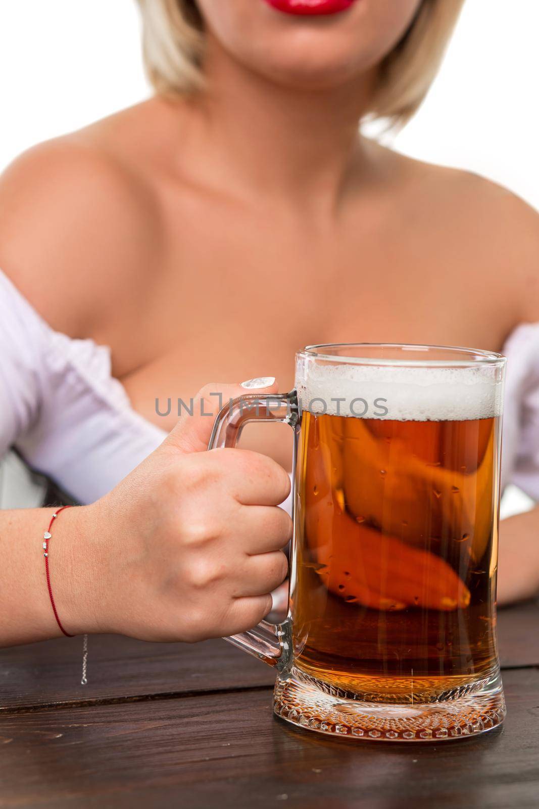 Beautiful young blond girl in dirndl drinks out of oktoberfest beer stein. Isolated on white background. sits by the table. close-up mug