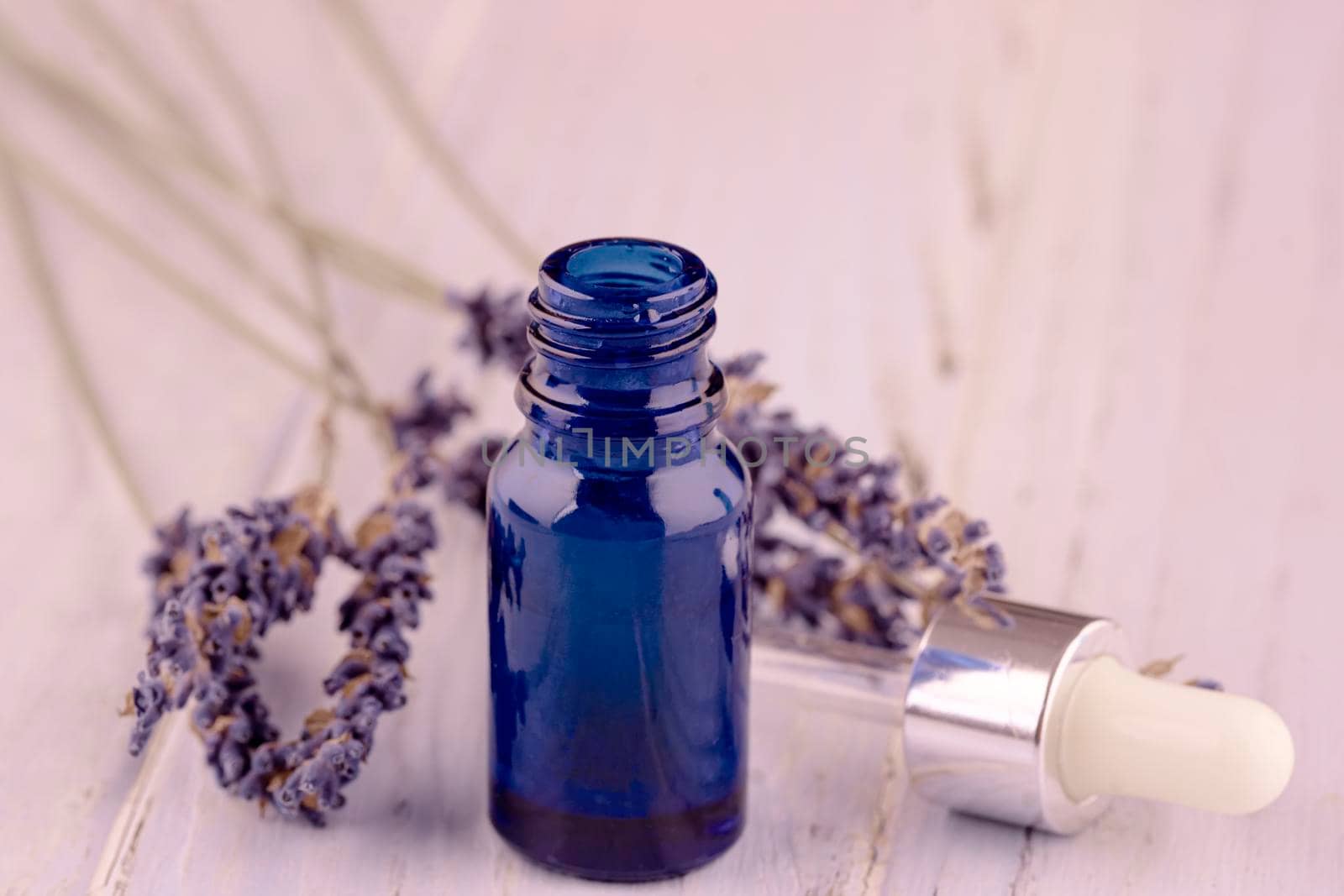 blue bottle of lavender massage oil on lavender wooden background by Iryna_Melnyk
