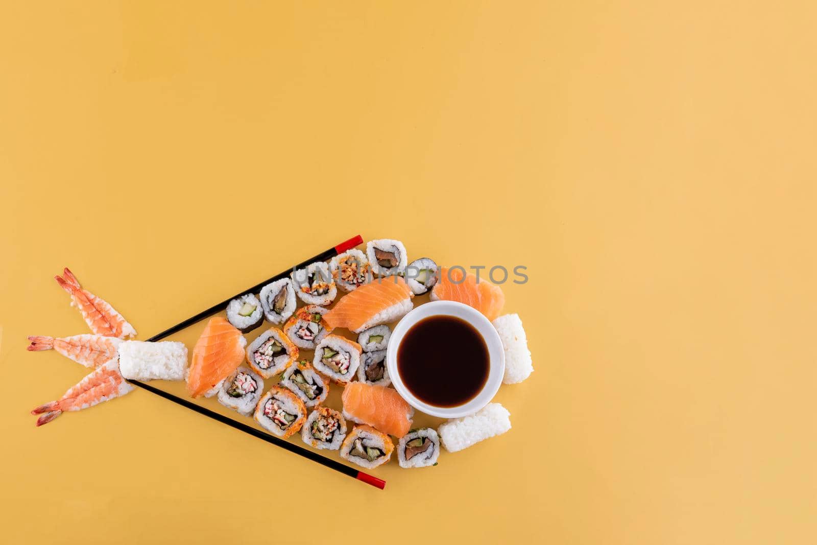 a set of sushi and soy sauce on a white plate in the form of fish ready to eat on a yellow background Space for text by Iryna_Melnyk