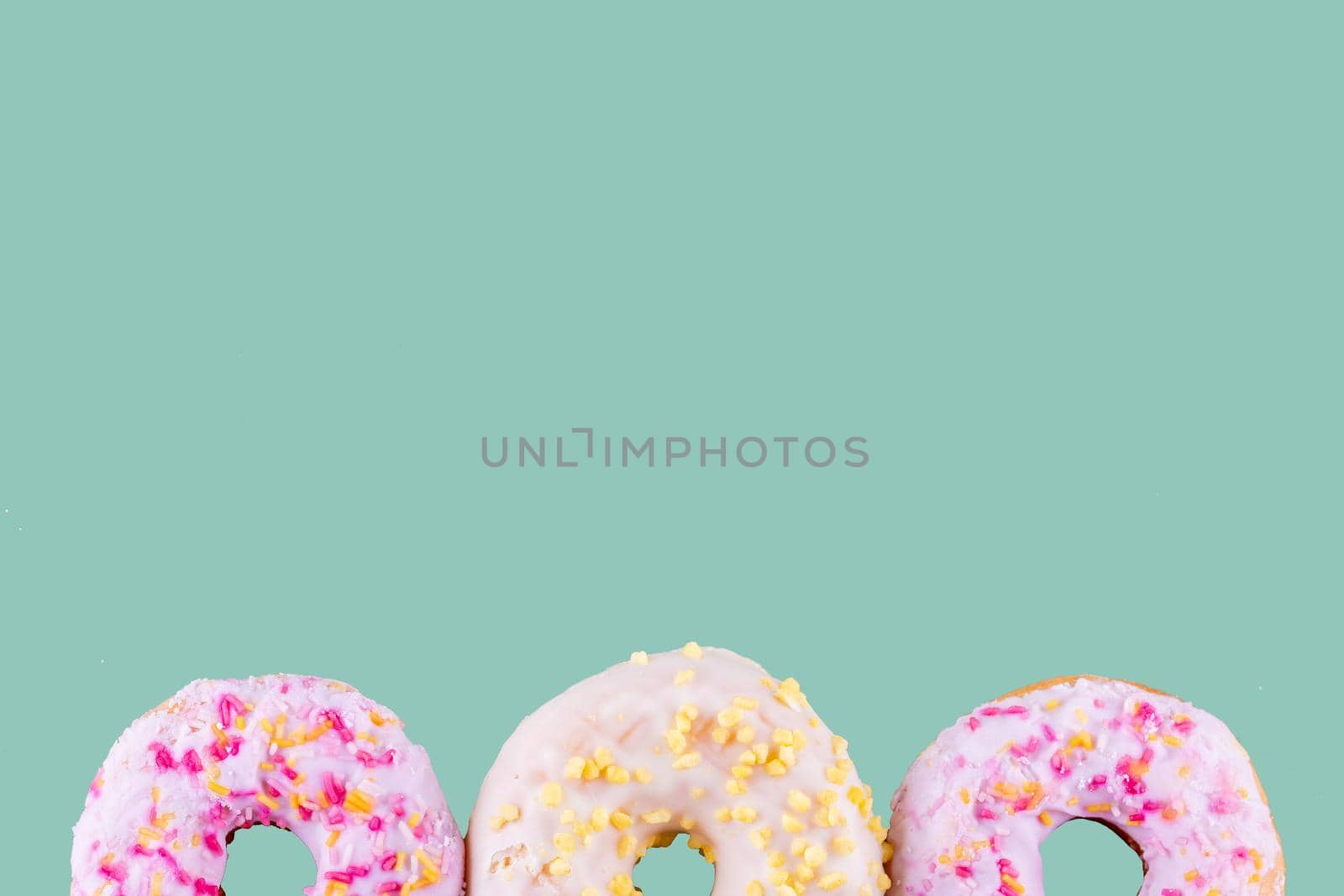 pink and yellow spricled donuts on a green background Space for text high-quality photos for calendar and cards