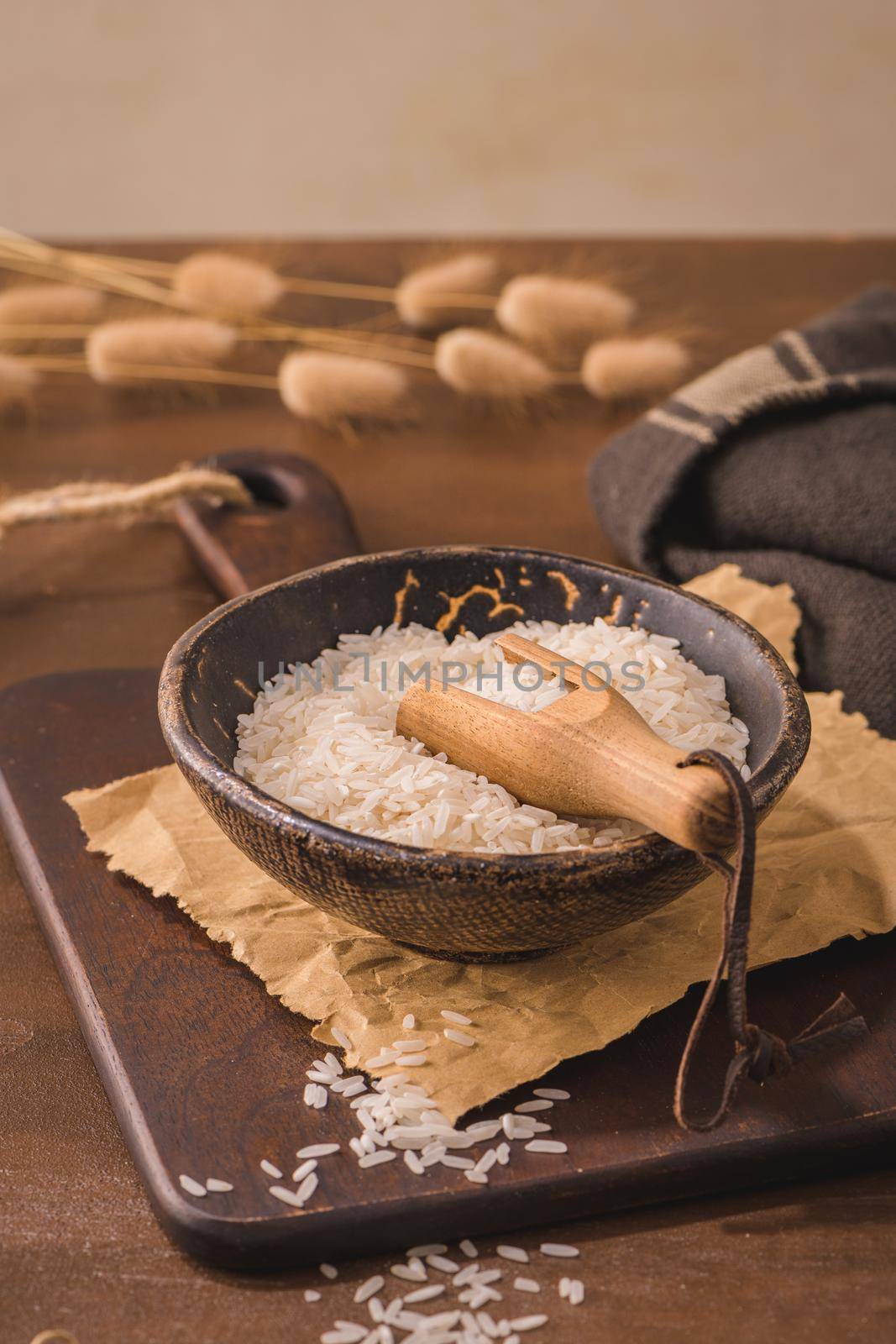 Long grain rice in ceramic bowl with wooden scoop on rustic countertop.
