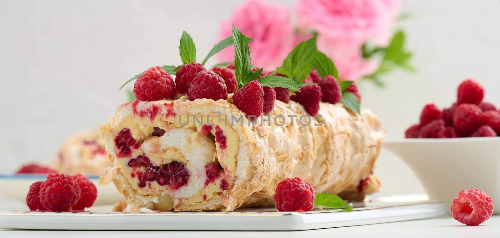 Baked meringue roll with cream and fresh fruits on a white wooden board, delicious dessert