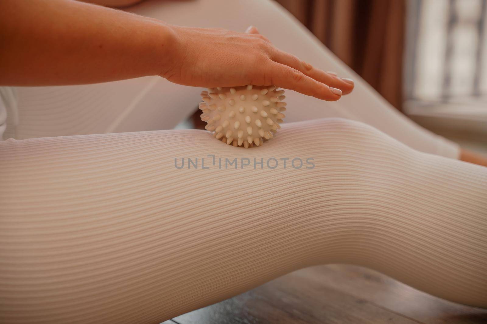 Athletic slim caucasian woman doing thigh self-massage with a massage ball indoors. Self-isolating massage.