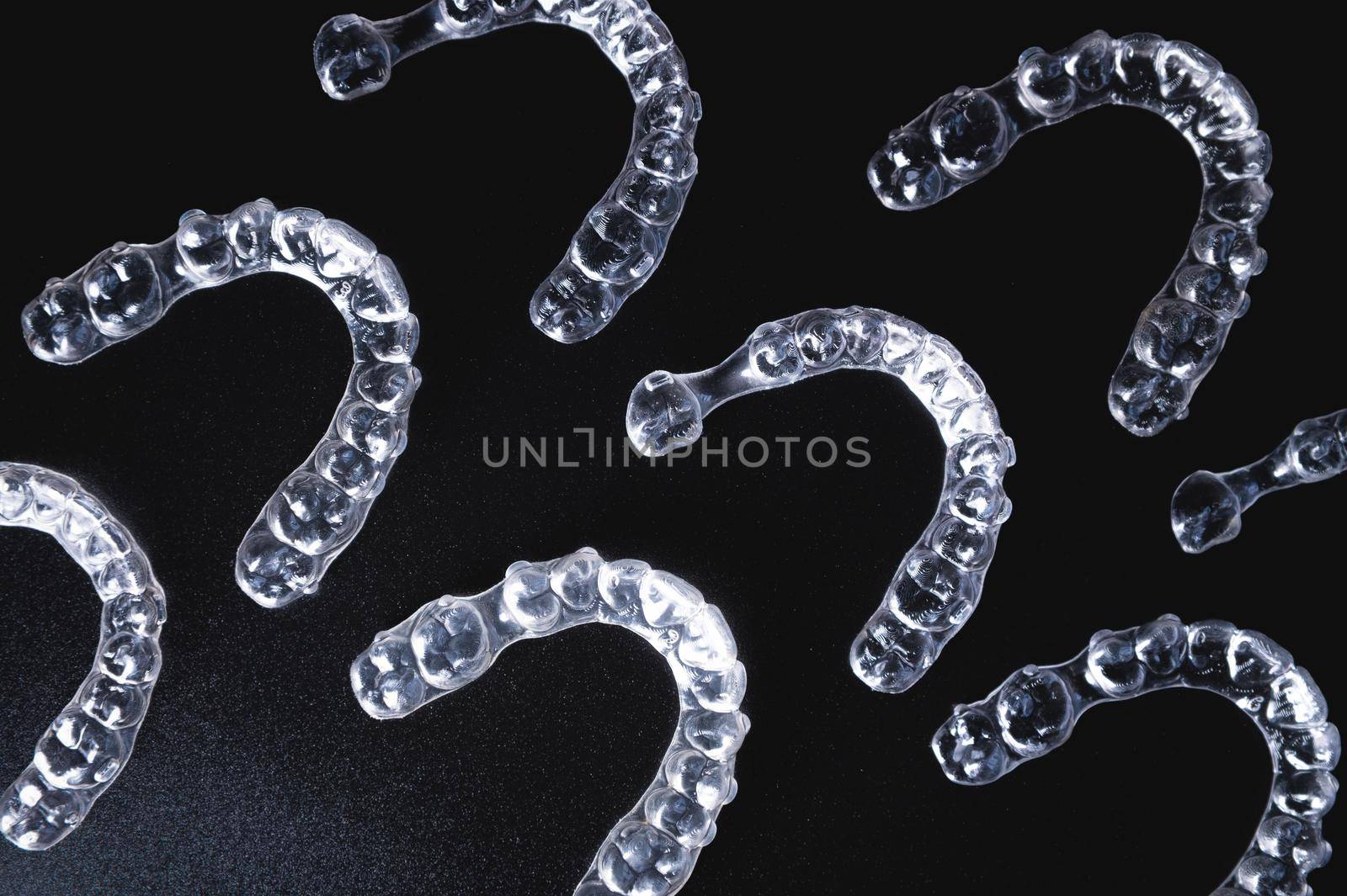 a pattern of invisible plastic aligners lie on a black background.