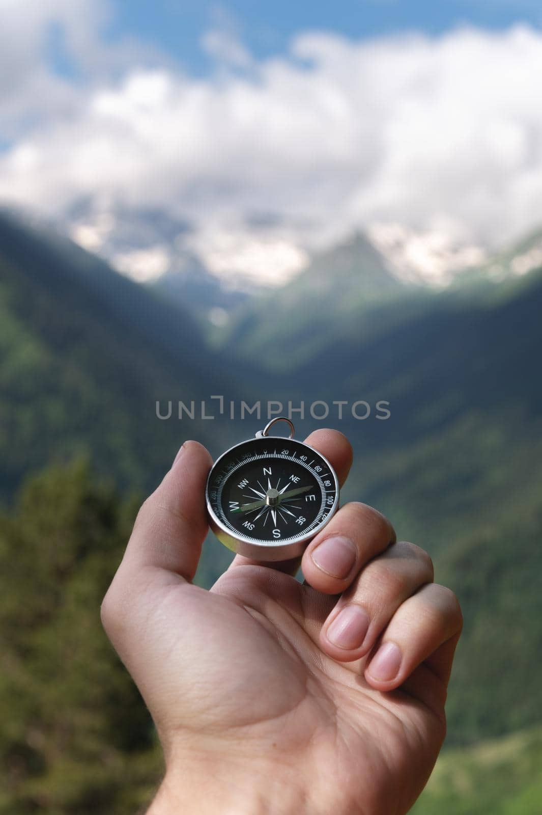 Magnetic compass in the palm of a male hand against the backdrop of a mountain range in the clouds in the summer outdoors, travel, first-person view by yanik88