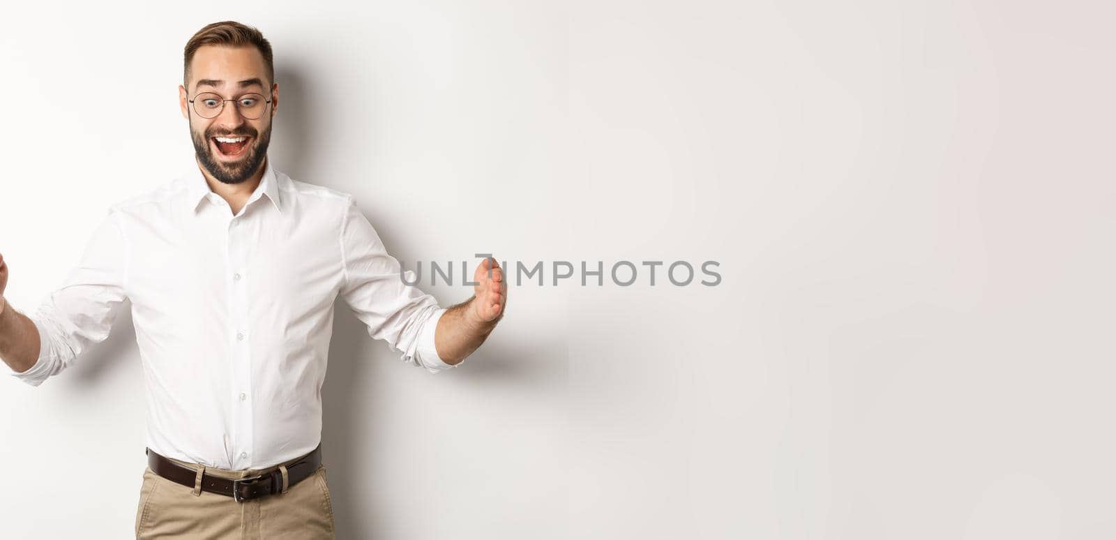 Amazed businessman showing big object, describe something large and looking excited, standing over white background.