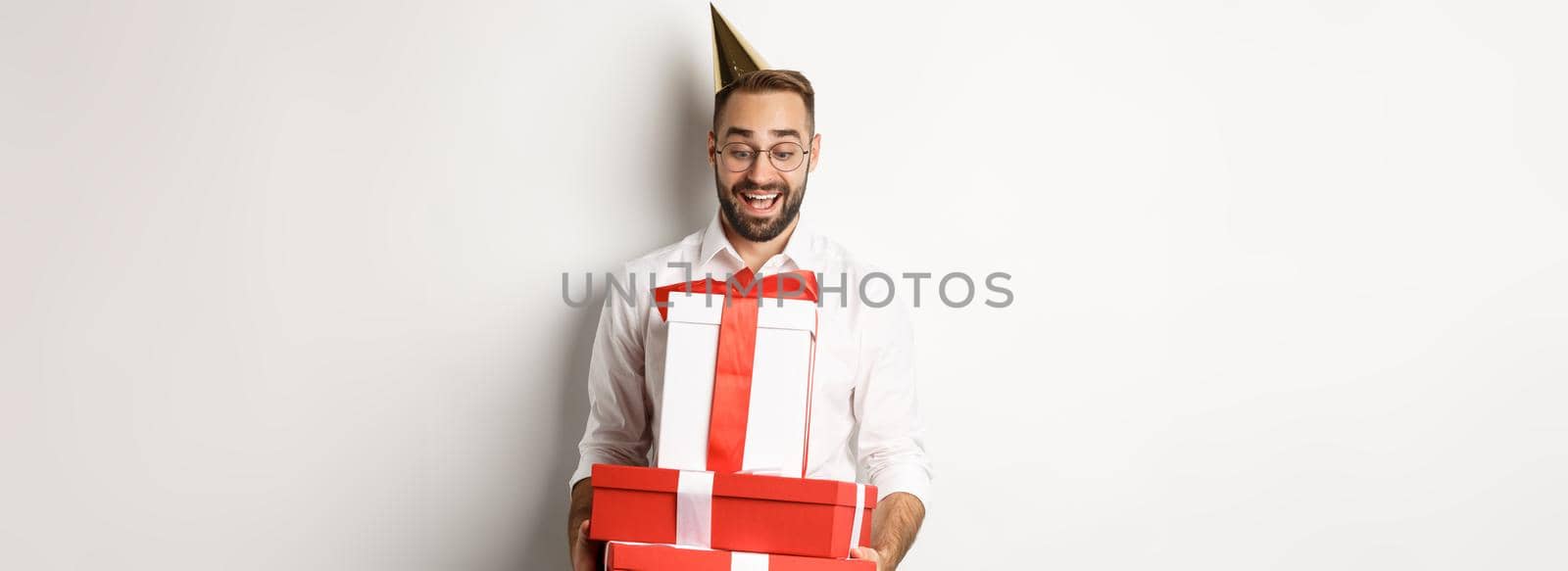 Holidays and celebration. Excited man having birthday party and receiving gifts, looking happy, standing over white background by Benzoix