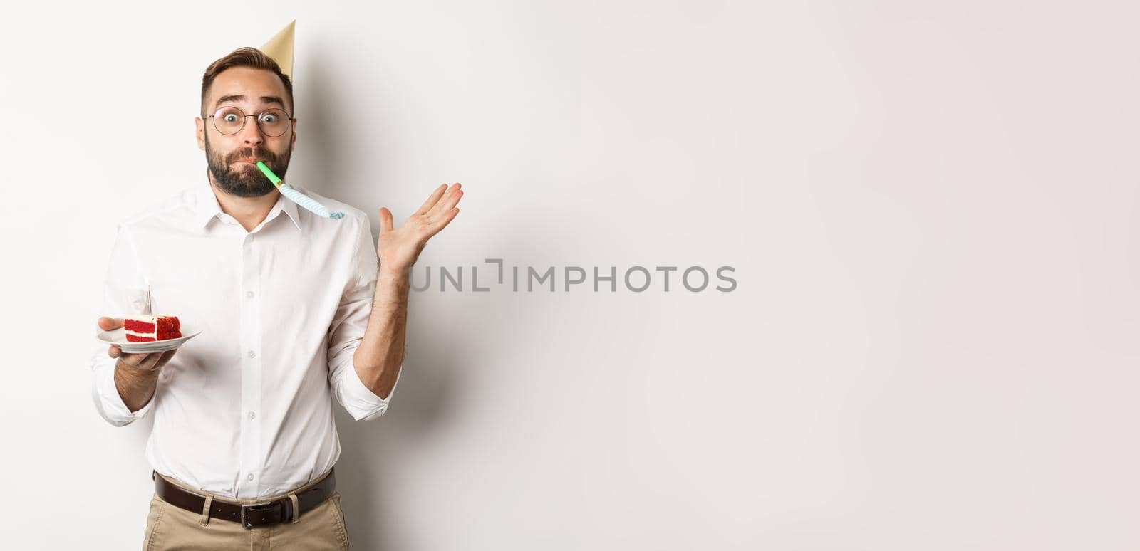 Holidays and celebration. Cheerful man enjoying birthday, blowing party whistle and holding bday cake, white background.