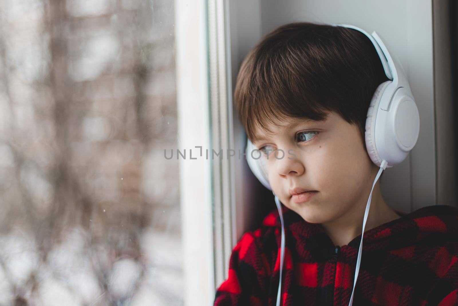 A boy with headphones looks out the window . Modern children. Social media. An article about modern children. Online fairy tales.