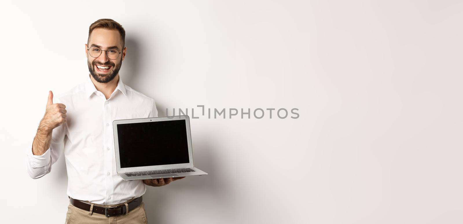 Successful business man showing laptop screen, make thumb up in approval, praise something good, standing over white background.