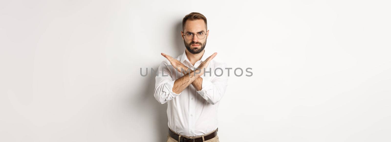 Angry businessman frowning and showing cross, stop you, telling no and prohibit something, standing over white background.
