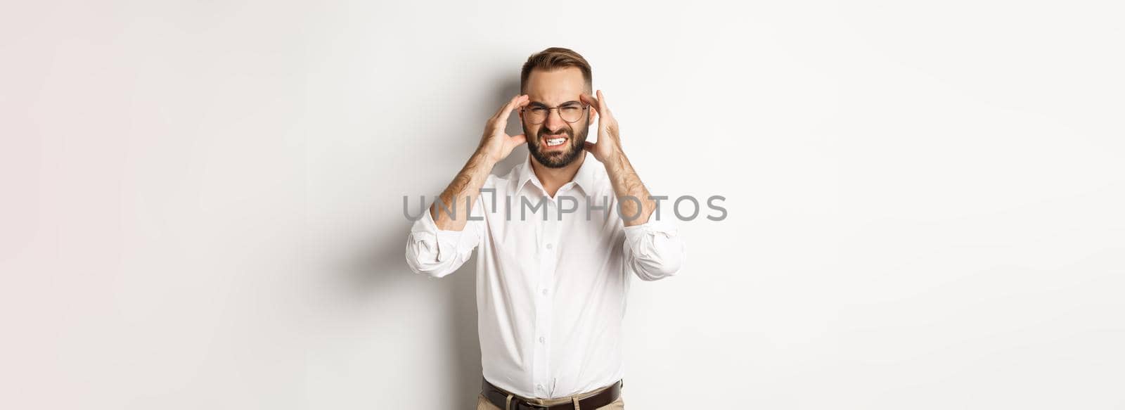 Businessman having headache, grimacing and holding hands on head, standing over white background by Benzoix