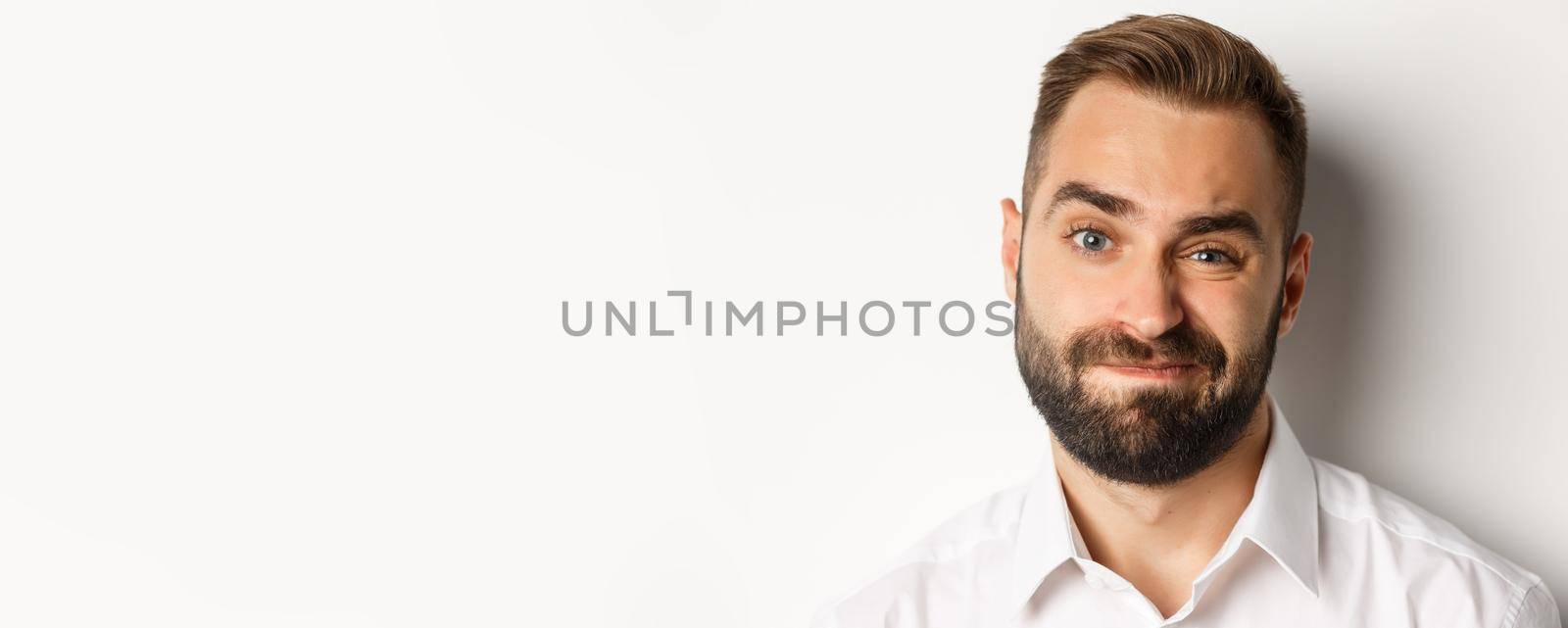 Emotions and people concept. Headshot of skeptical man with beard, grimacing and looking doubtful, standing displeased against white background by Benzoix