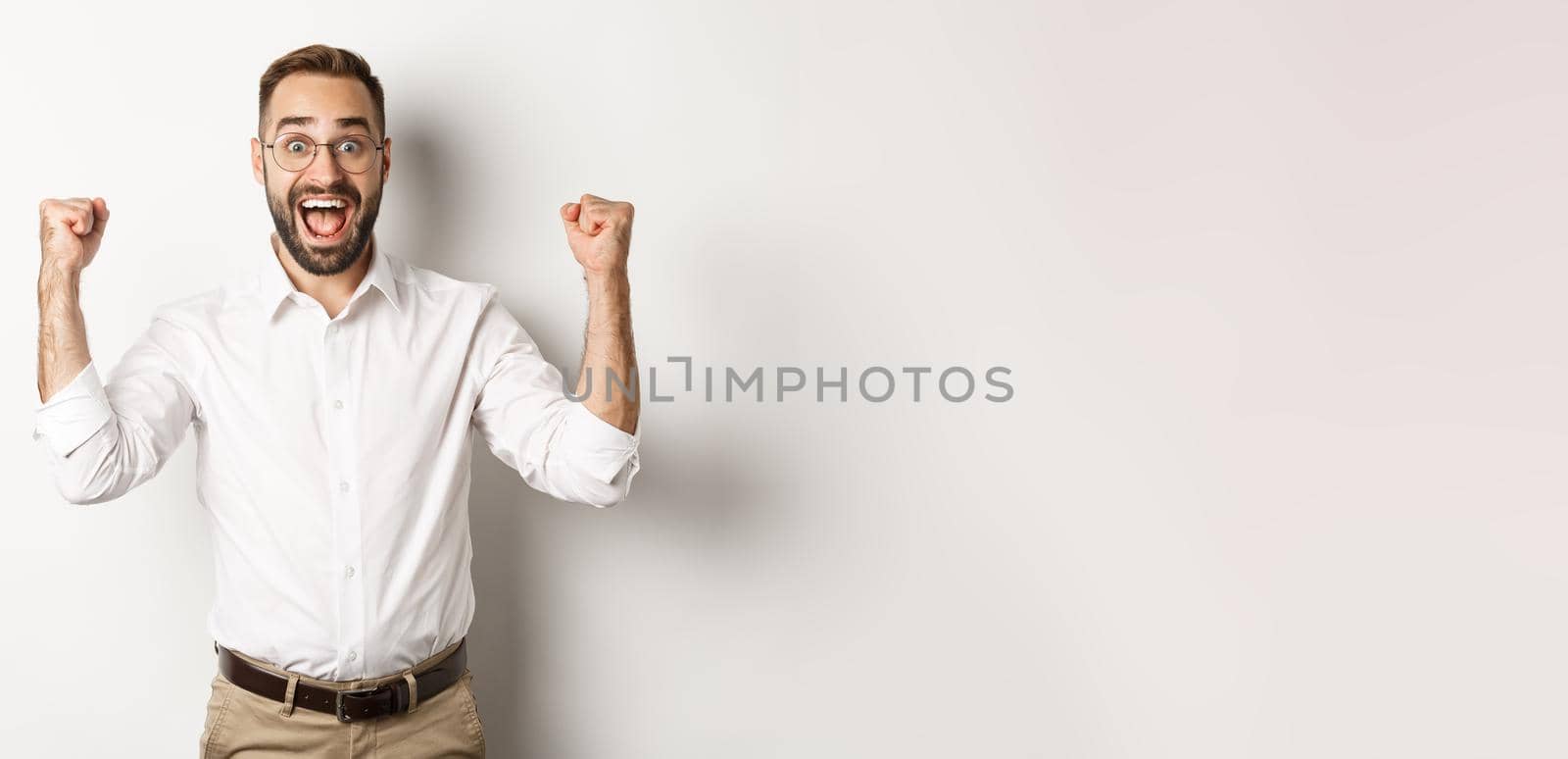 Successful businessman rejoicing, raising hands up and celebrating victory, winning something, standing over white background by Benzoix