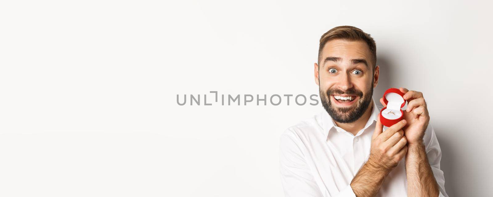 Close-up of handsome guy making proposal, looking hopeful and showing wedding ring, asking marry him, white background.