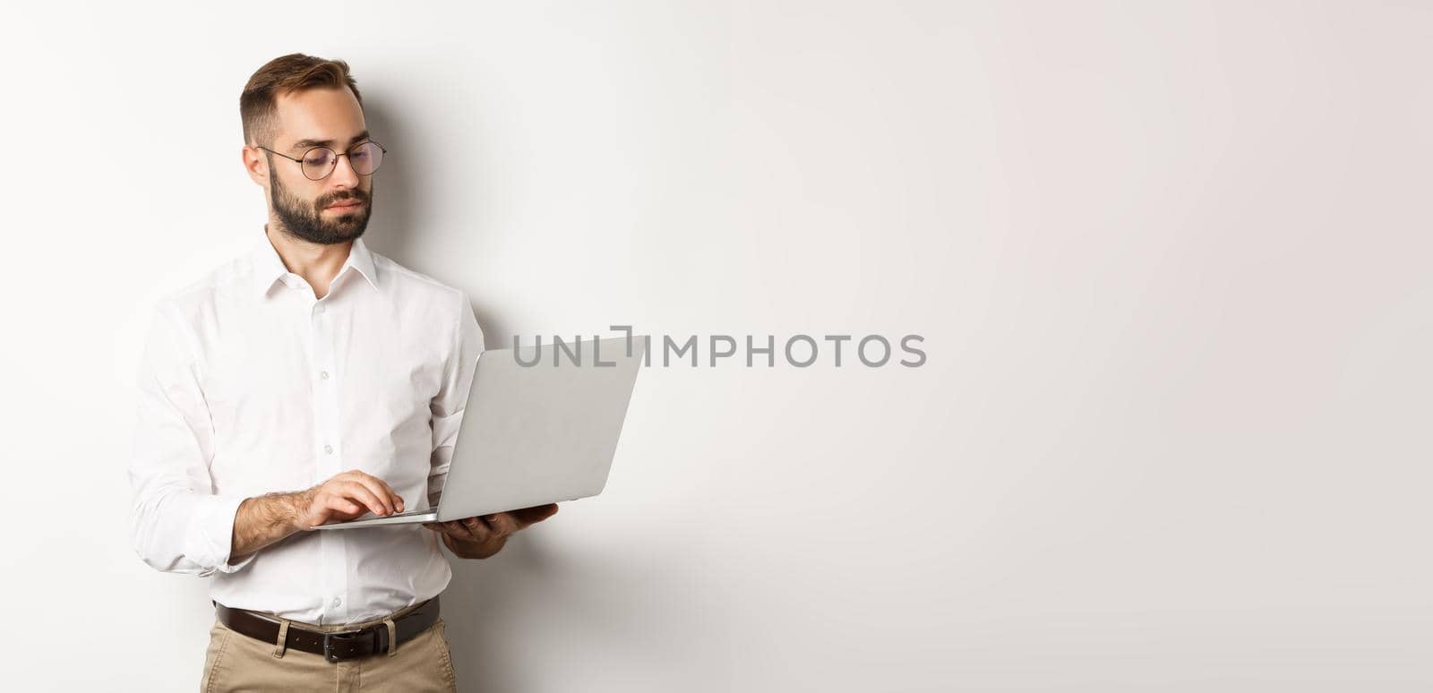 Business. Serious manager working on laptop, standing over white background. Copy space