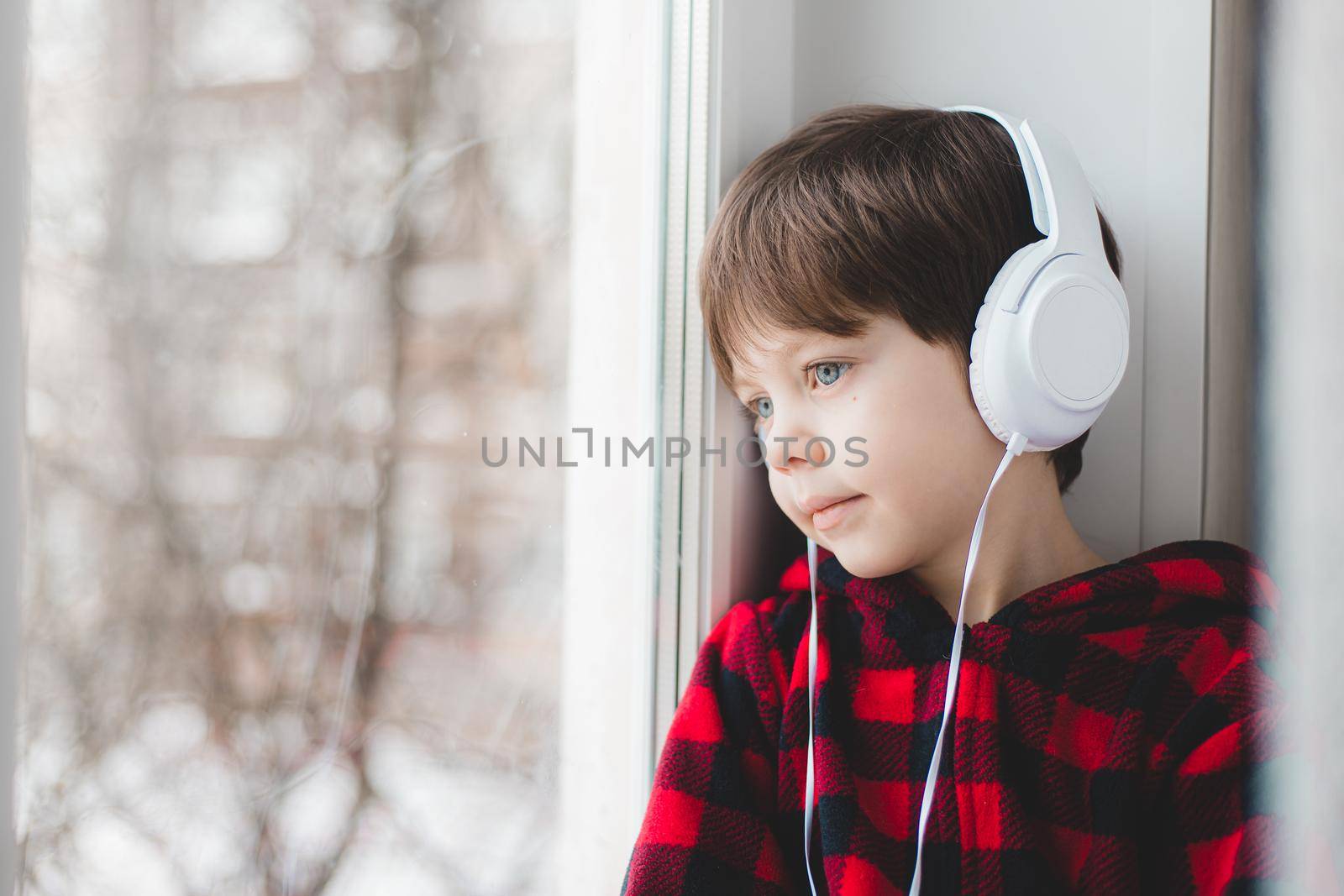A boy with headphones looks out the window . Modern children. Social media. An article about modern children. Online fairy tales.