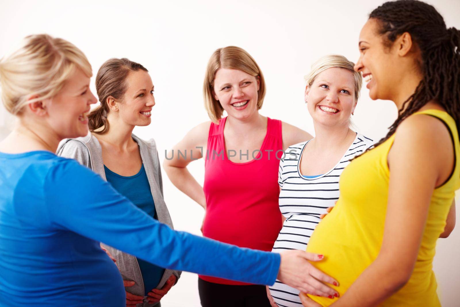 Hes a kicker. A young woman touching her pregnant friends belly while they stand in a group having a friendly discussion. by YuriArcurs