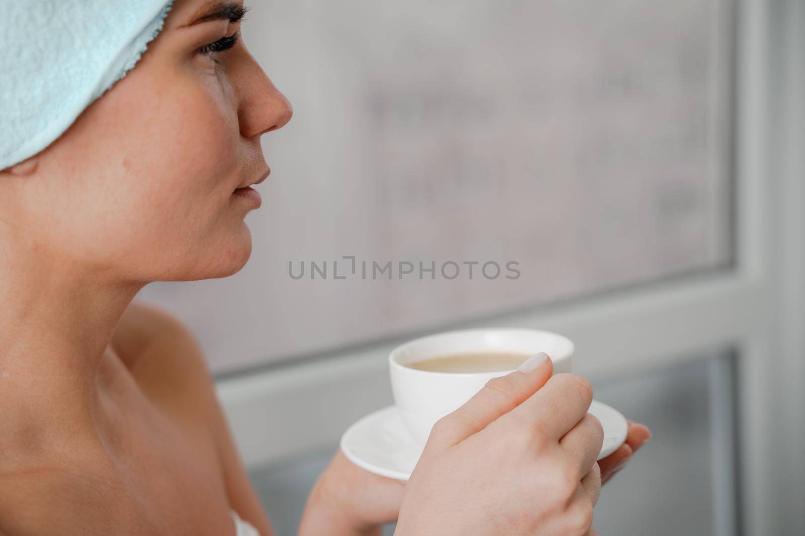 Young serene relaxed woman in spa bath towel drinking hot beverage tea coffee after taking shower bath at home. Beauty treatment, hydration concept