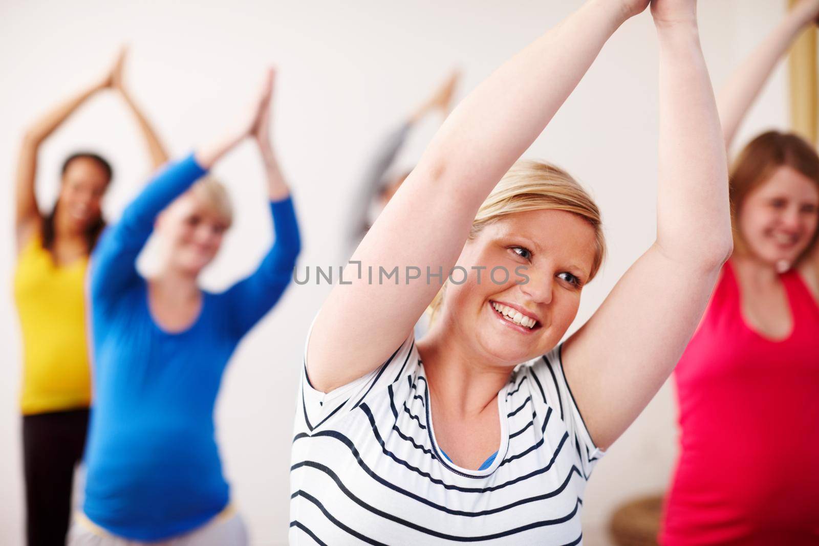 Joyful yoga. A multi-ethnic group of pregnant women doing exercises with their arms stretched upwards. by YuriArcurs