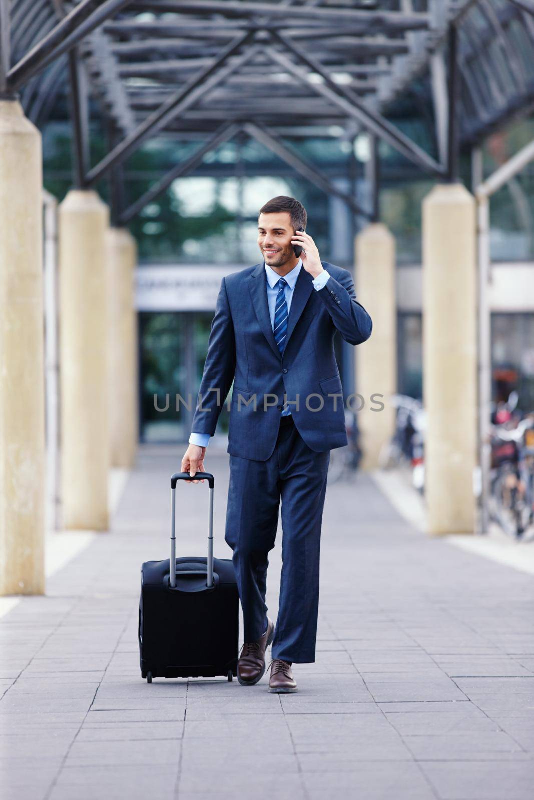 Business communication as he commutes...A handsome young businessman on his mobile while walking into the airport with his luggage
