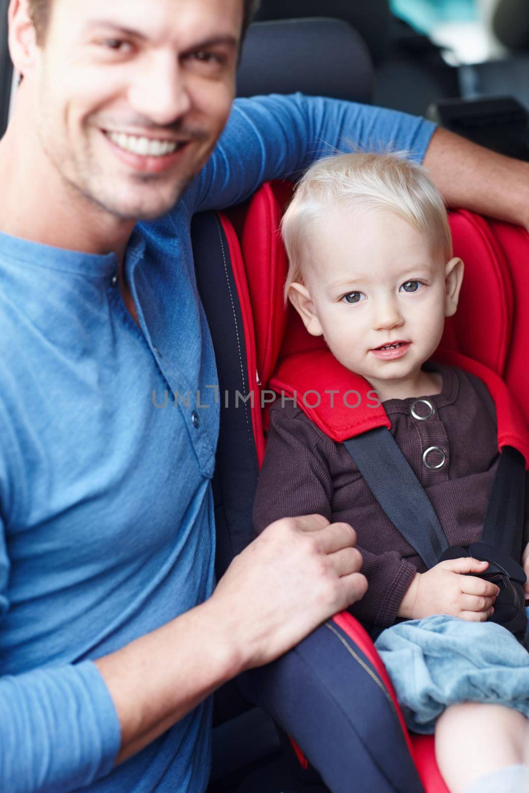 Looking after my son. Portrait fo a smiling father next to his toddler who is sitting in his baby seat