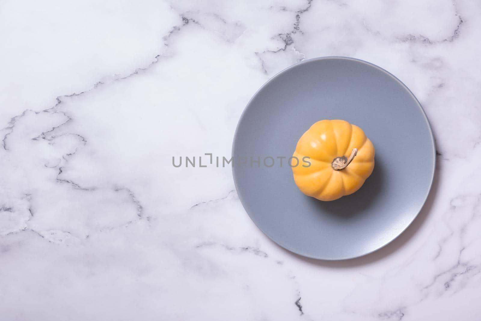Orange pumpkin on a blue plate from above. Minimalist concept of the autumn menu.