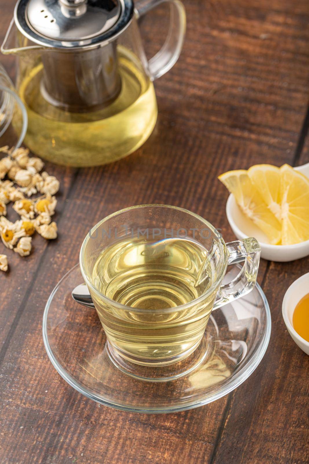 Relaxing chamomile tea in glass cup with lemon slices and honey next to it on wooden table.