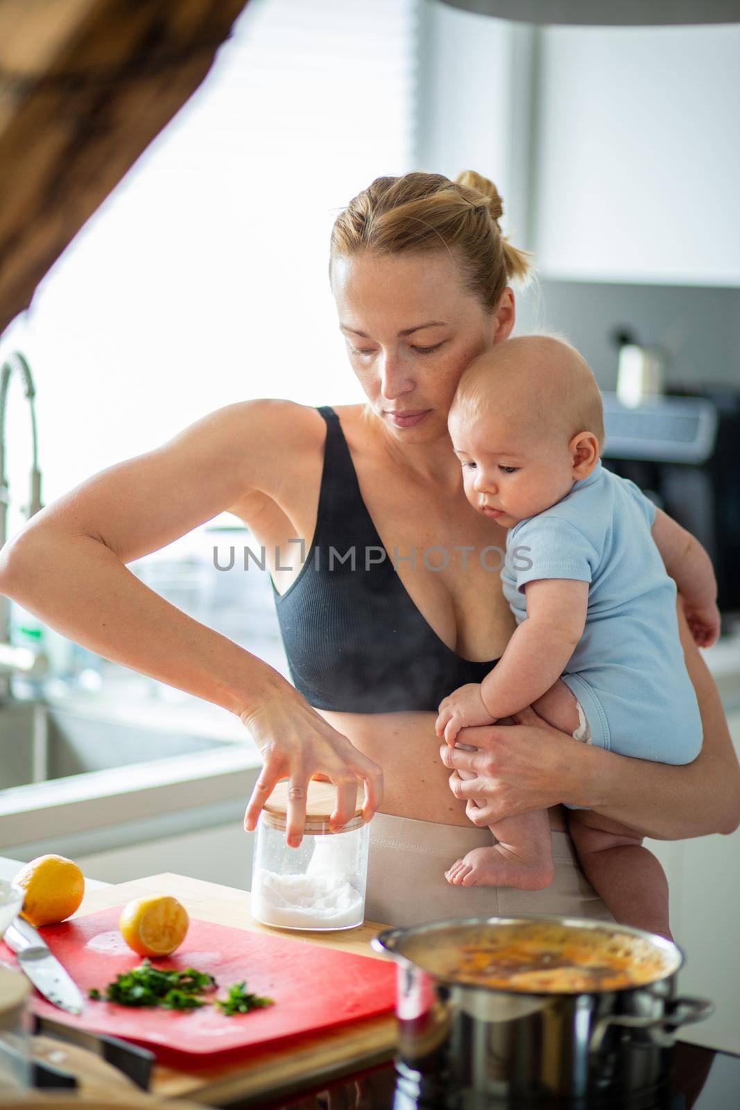 Woman cooking while holding four months old baby boy in her hands.
