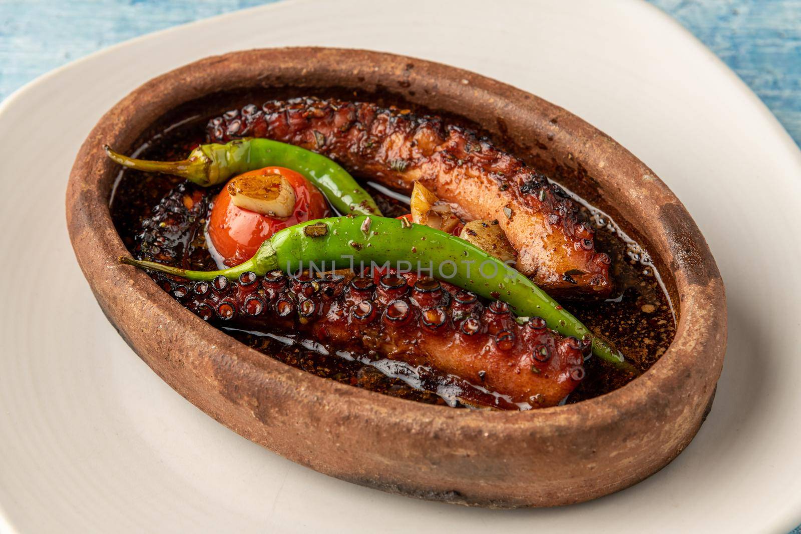 Casserole octopus with tomatoes and peppers on blue stone background by Sonat