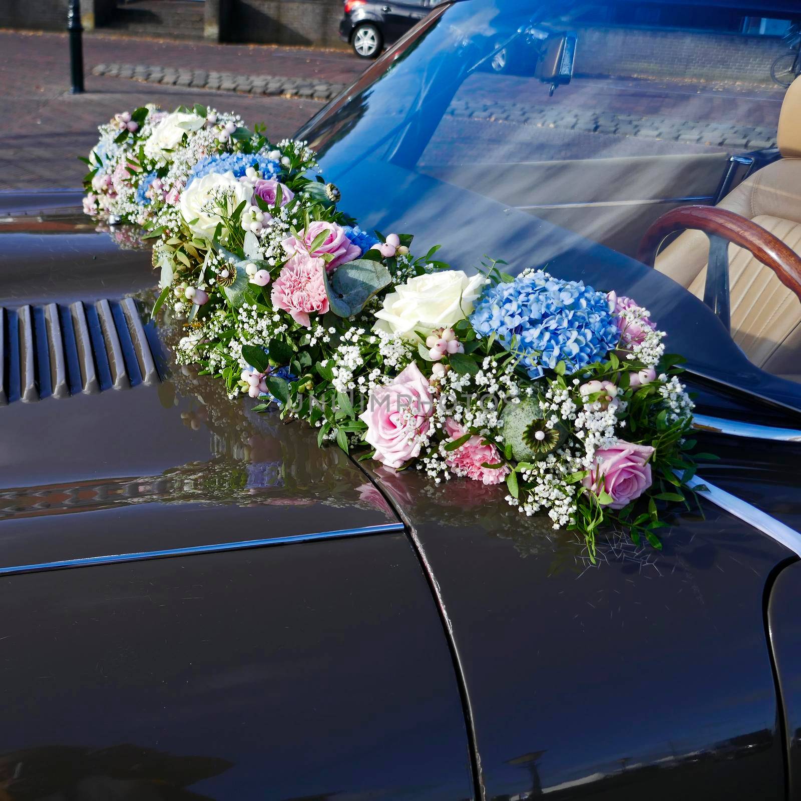 A flower-decorated car for a wedding. It's a classic brown convertible with a floral garland between the hood and the windshield