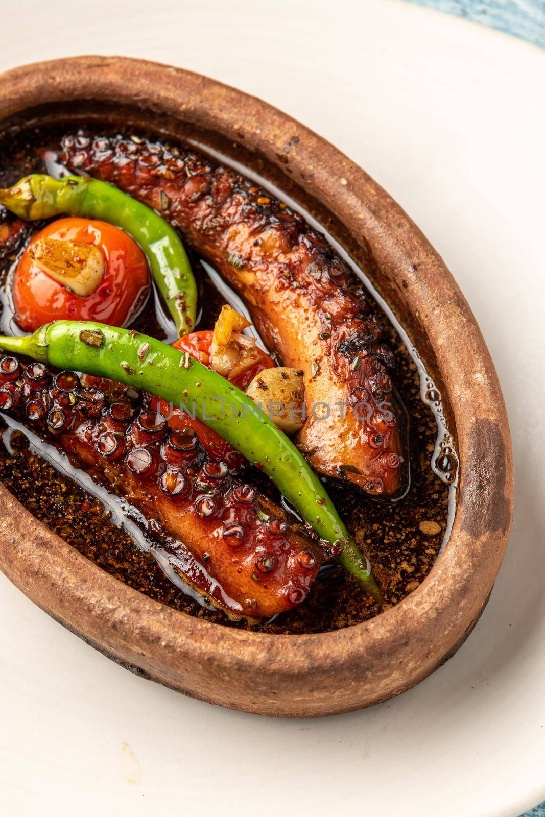 Casserole octopus with tomatoes and peppers on blue stone background