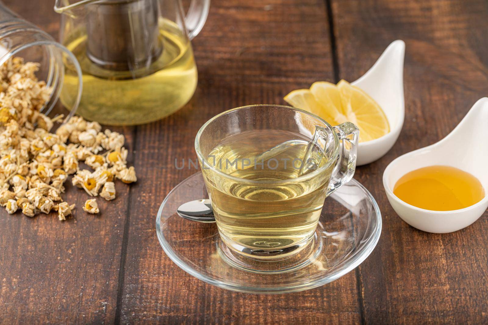 Relaxing chamomile tea in glass cup with lemon slices and honey next to it on wooden table. by Sonat