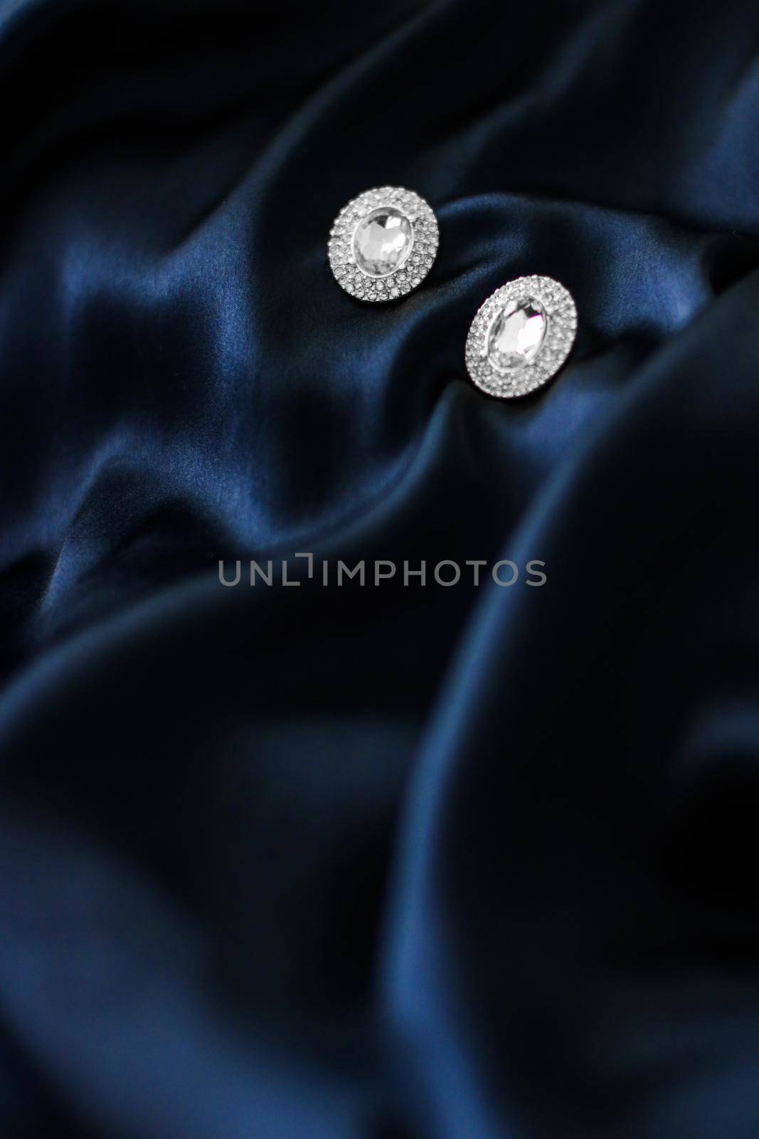 Luxury diamond earrings on dark blue silk background, holiday glamour jewelery present by Anneleven