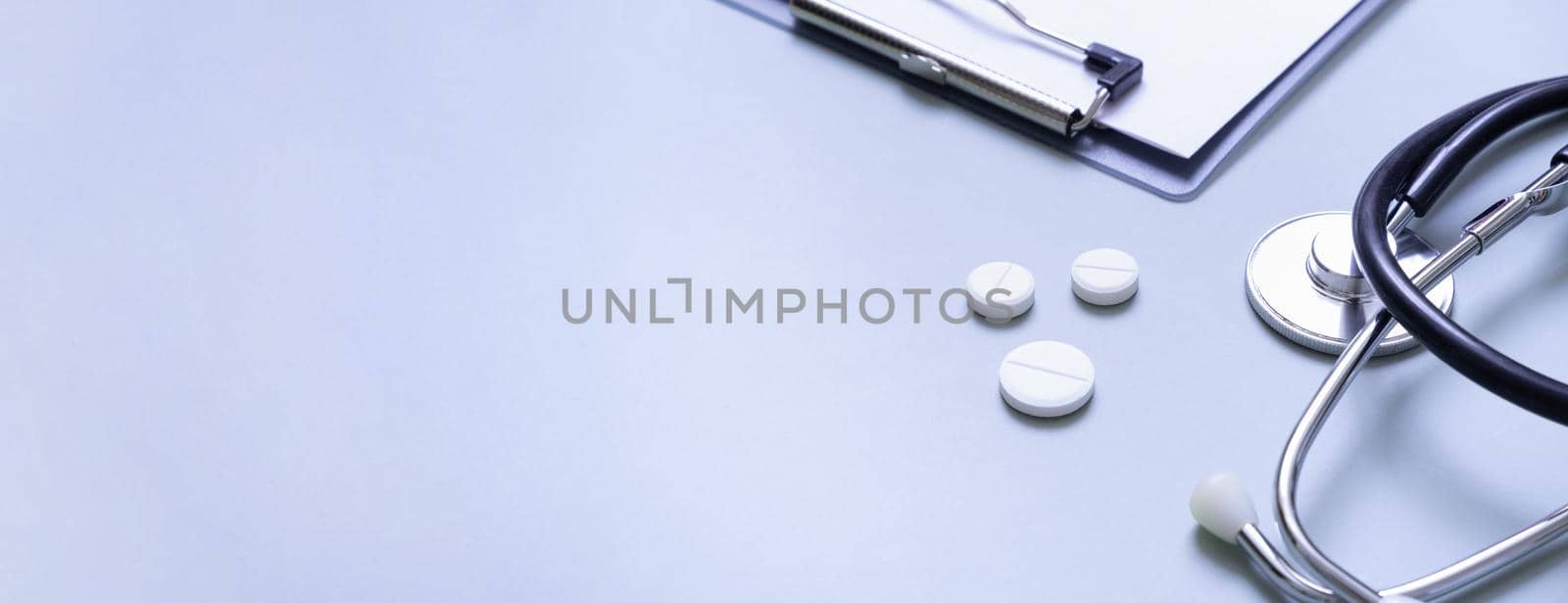 Banner with stethoscope, pills and tablet at doctor's workplace on colored background with copy space.