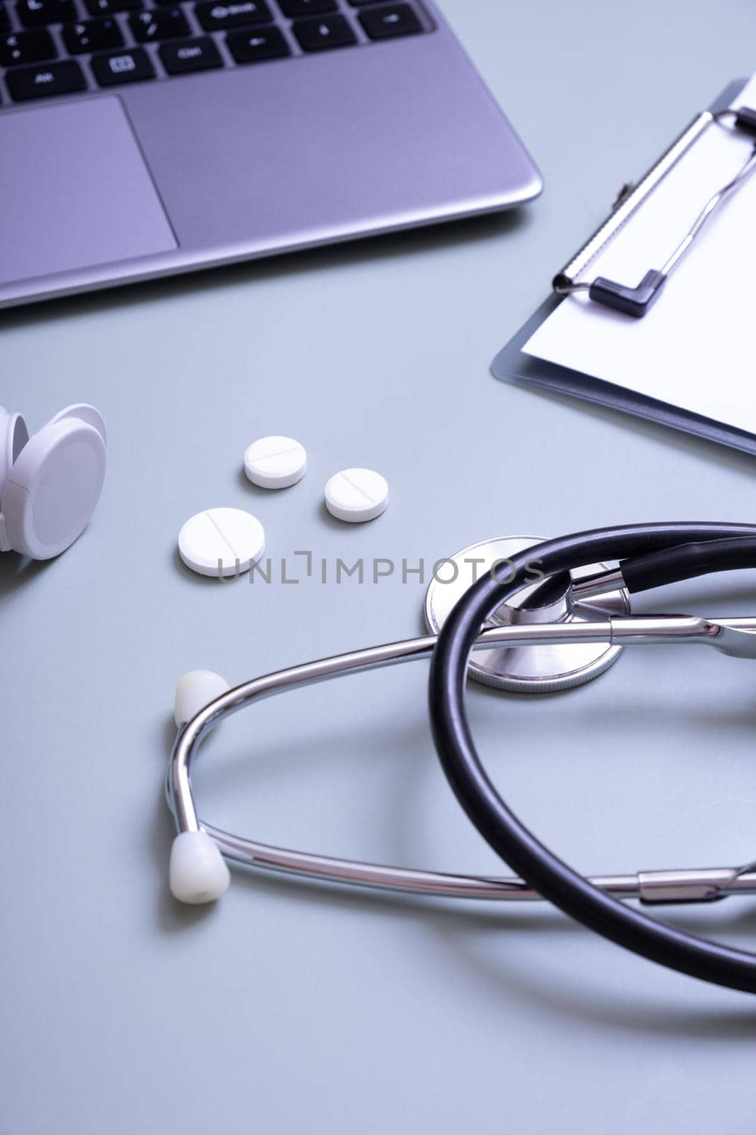 Stethoscope, pills with a container on the desktop on the background of a laptop and a tablet