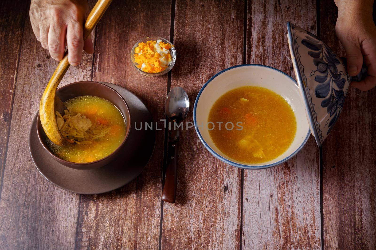 woman serving chicken soup with a wooden spoon in a brown bowl on a wooden table