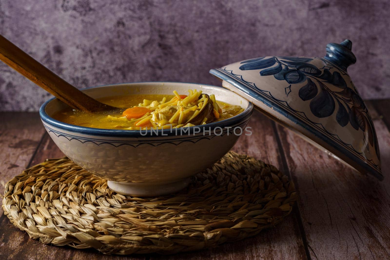 white and blue soup tureen with chicken noodle and vegetable soup with a wooden spoon